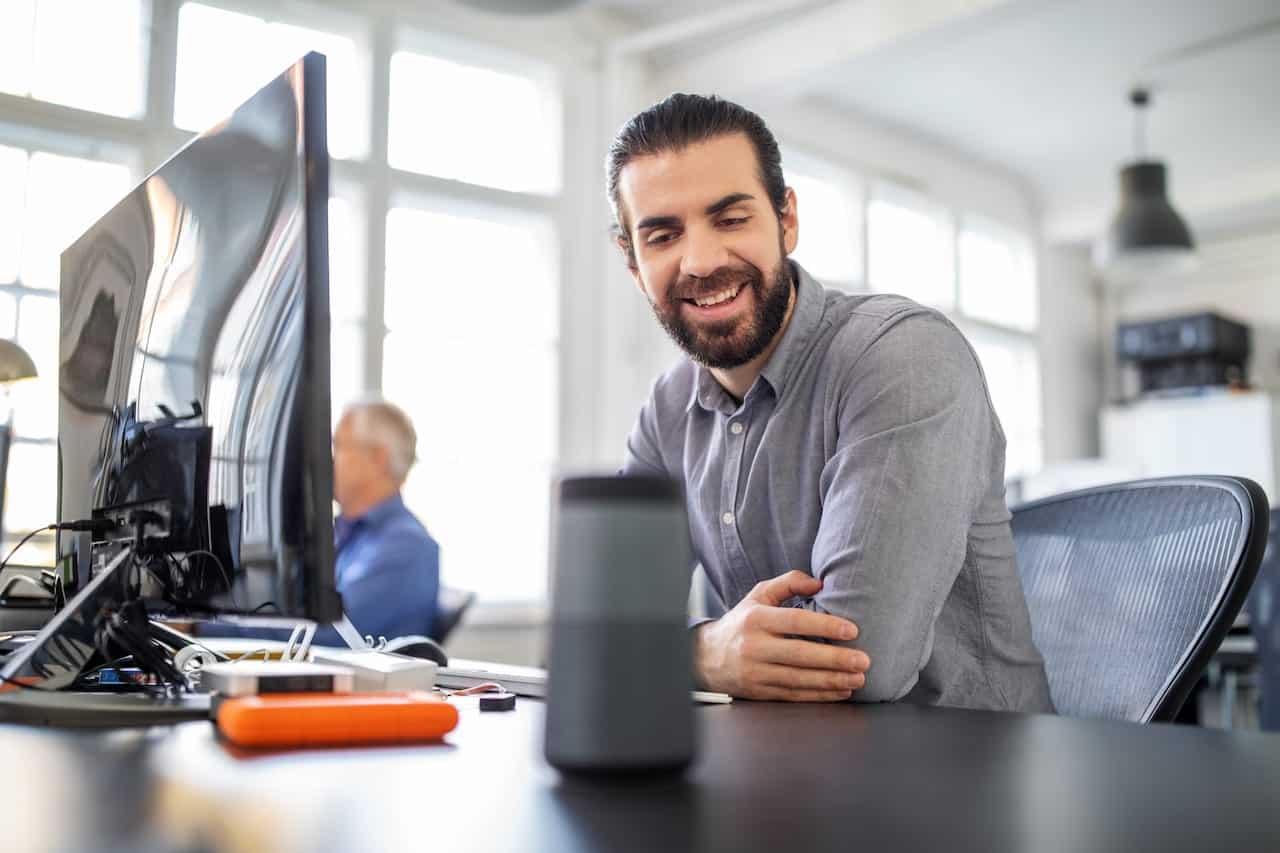 Businessman sitting at his desk talking to smart speaker. Male professional asking digital assistant a question at office.