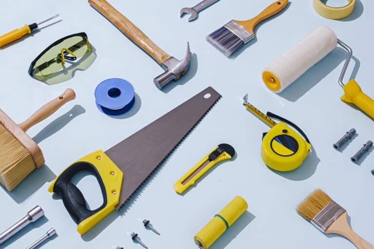 A close-up image of various construction tools spread out on a blue workbench. The tools are neatly arranged and include a hammer, saw, tape measure, level, and screwdriver. In the background, a blurred shelf holds additional tools and hardware, representing the tools needed to get back to customer experience basics.