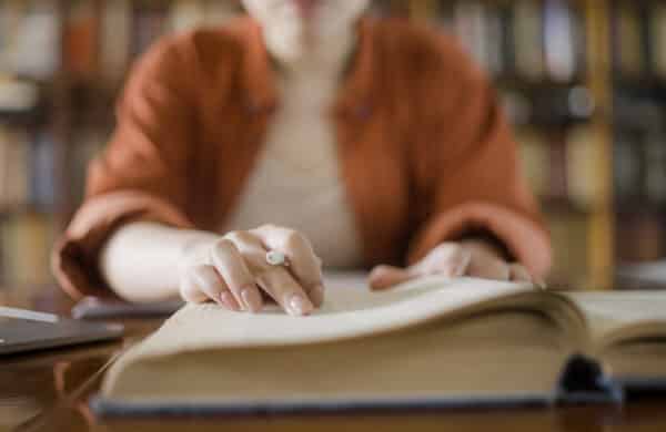 Woman reading book in library doing research, representing going beyond keywords to uncover semantic vector search meaning for better search and discovery experience.