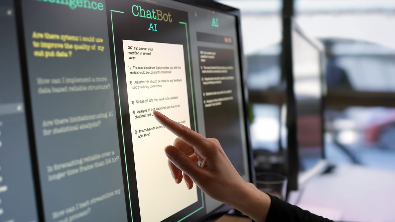 Close-up stock photograph showing a touchscreen monitor being used in an open plan office. A woman’s hand is asking an AI chatbot pre-typed questions & the Artificial Intelligence website is answering. Representing private LLMs.