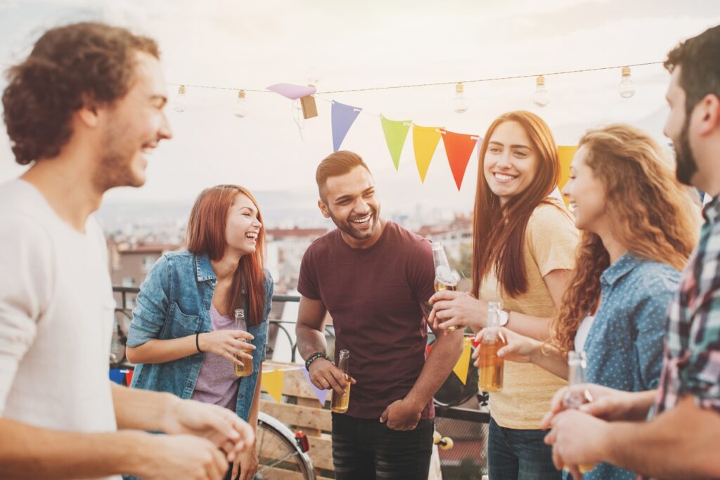 Multi-ethnic group of young people chatting and laughing on a rooftop party.