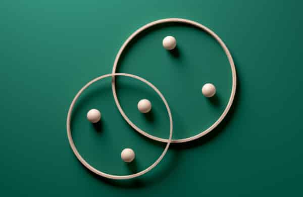 Two wooden rings interlocking with balls inside them on a green background. This image symbolizes the combination of traditional search methods with semantic understanding in hybrid search.