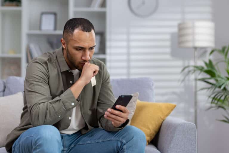 A young African American man looks concerned at his mobile phone, suggesting worry and discomfort with gen ai personalization.
