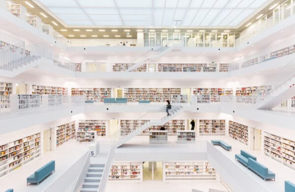 Large white library with many rows of bookshelves and a modern design with glass windows. [Large language models and search engines working together / Librarian using search engine to find information]