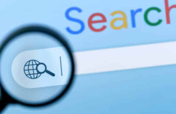 A magnifying glass hovers over the Google search bar, symbolizing the need for scrutiny and precision in AI-powered search results to avoid misinformation and "hallucinations."