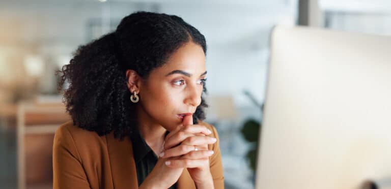A woman sits at a desk, deep in thought, surrounded by documents and a laptop. She is contemplating the strategic implementation of generative AI for knowledge management in her organization, weighing the risks and rewards of this transformative technology.