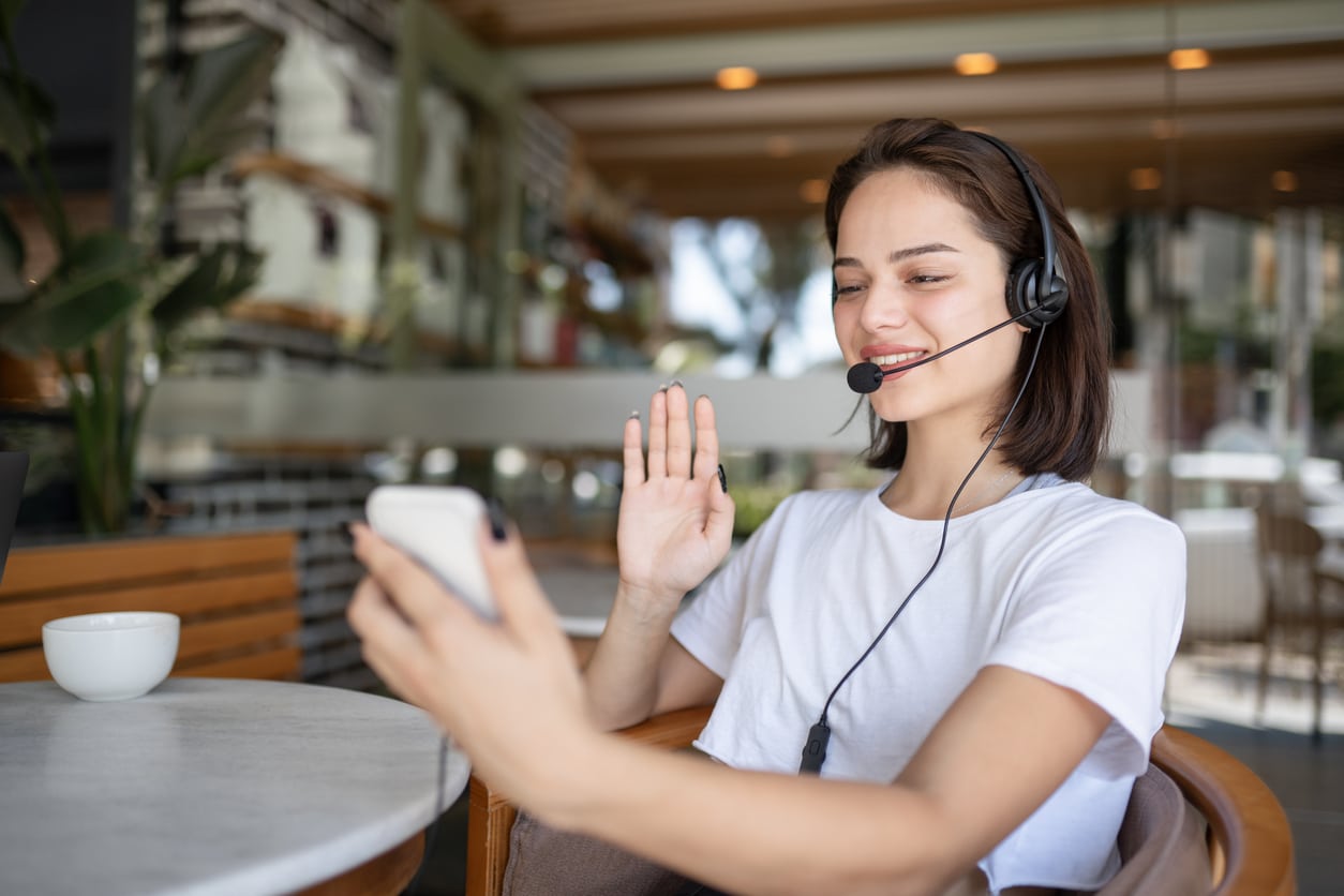 A female customer service representative working in a café setting, wearing a headset while engaging in a call. The woman is providing remote customer service, representing the modern work life that focuses on optimizing customer experience in a relaxed environment.