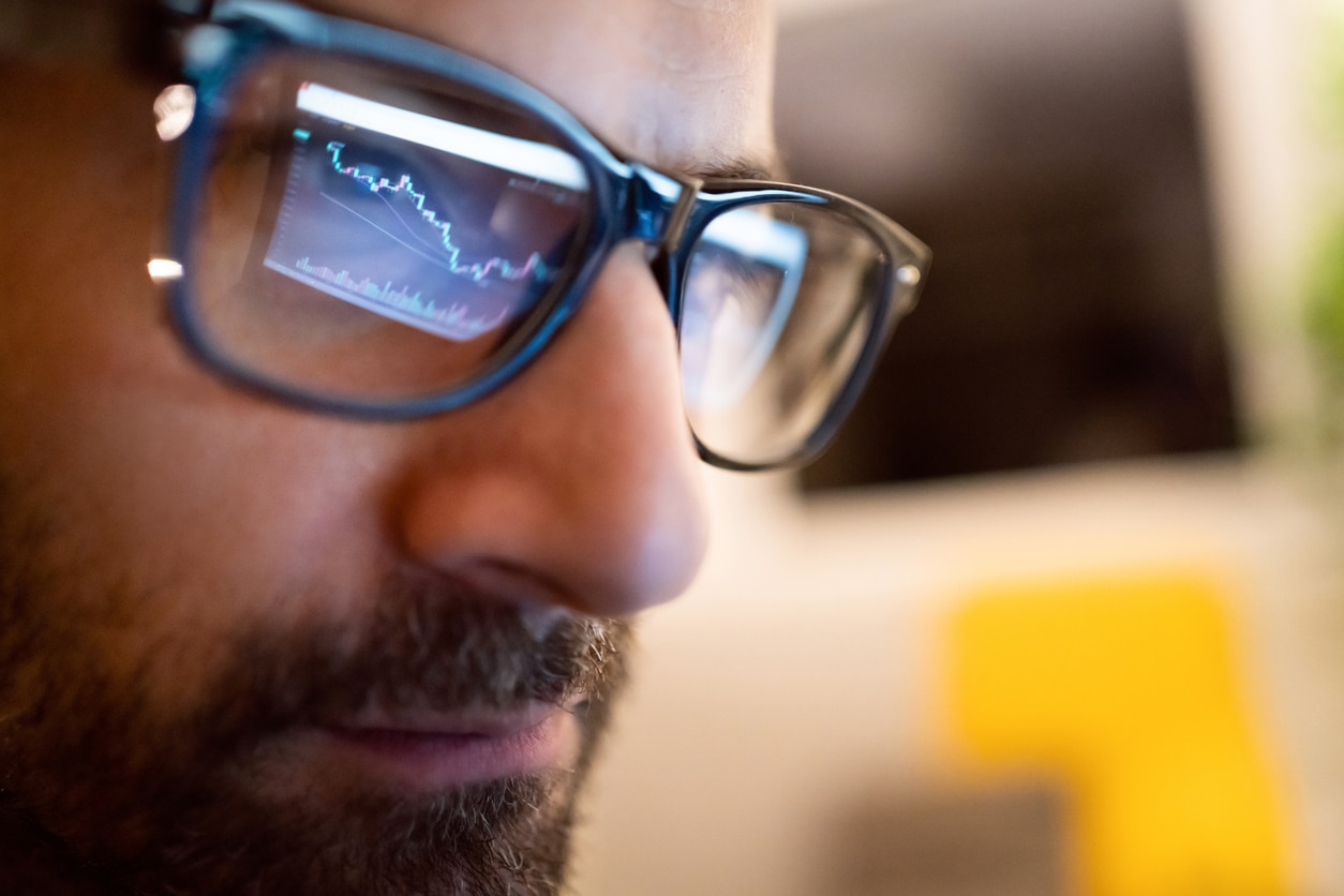 Close up of eyeglass reflection of a focused male Caucasian trader follow the crypto graph on laptop